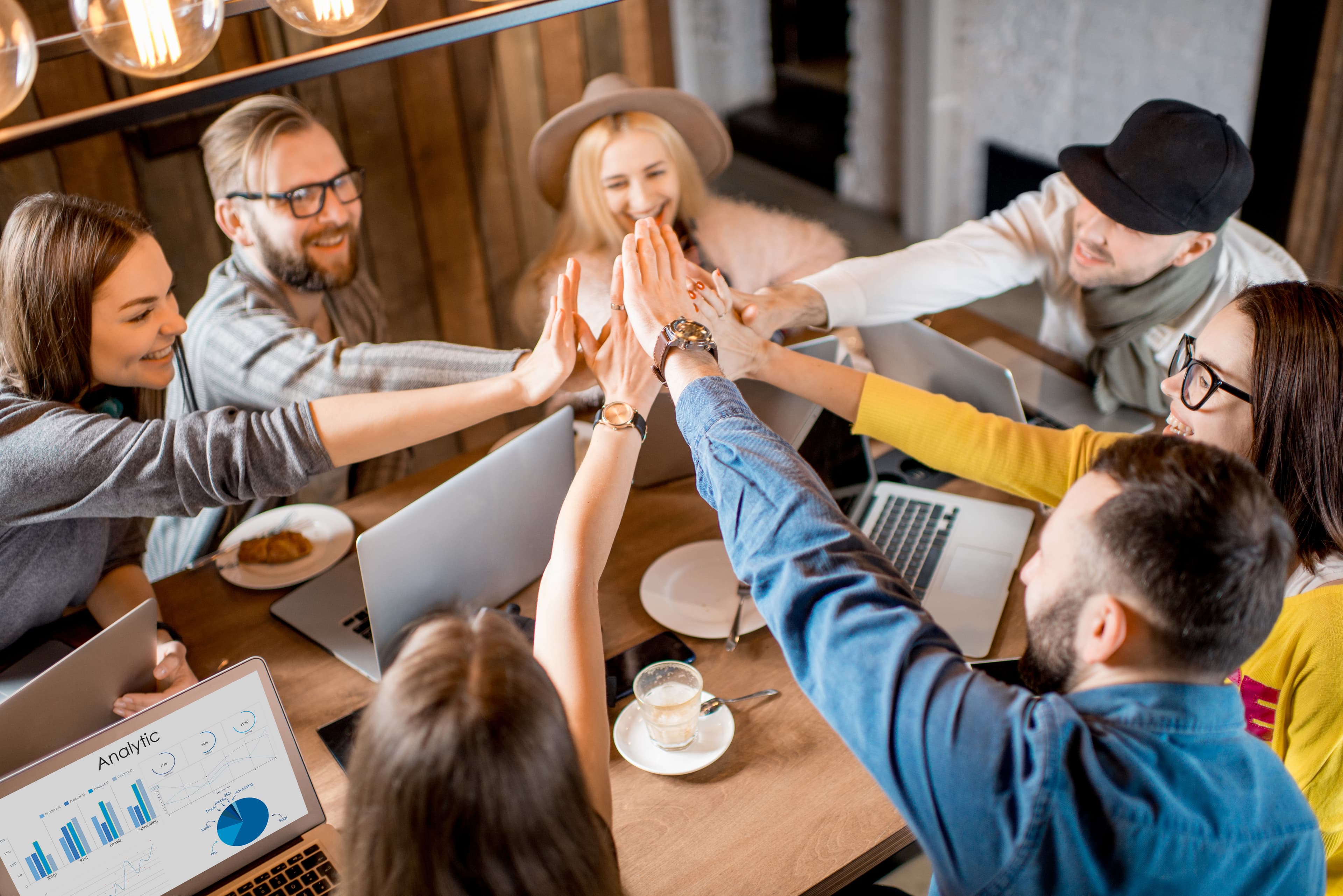 Diverse team celebrating successful onboarding with high-five around laptops